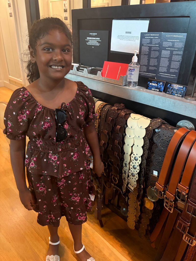 Riya smiling next to the Lucky Brand checkout shelf where TNT Detail Pros cards are displayed