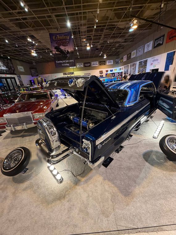 Rear of a dark blue lowrider Impala with chrome details at a car show