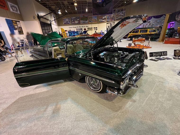 Dark green lowrider with the hood and door open at a car show