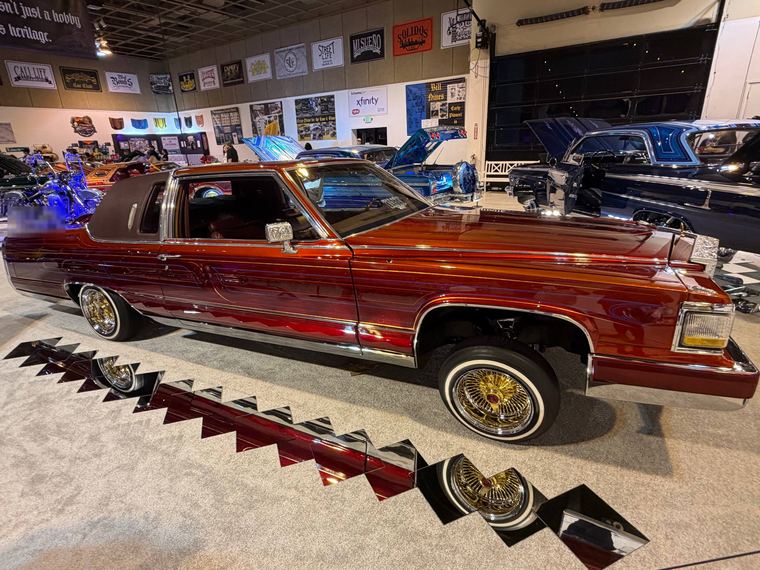 Candy red lowrider Cadillac with gold wire wheels at a car show
