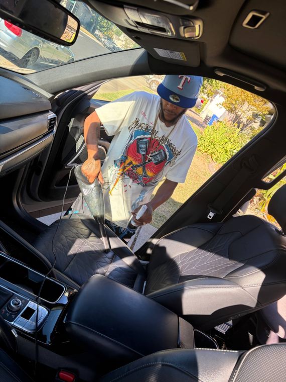 Tommy vacuuming the seats of a black leather interior and spraying cleaner